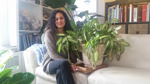 woman sits on a couch with a thriving house plant